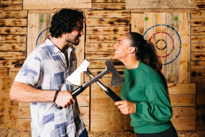 Two people holding axes, smiling playfully in front of wooden targets.