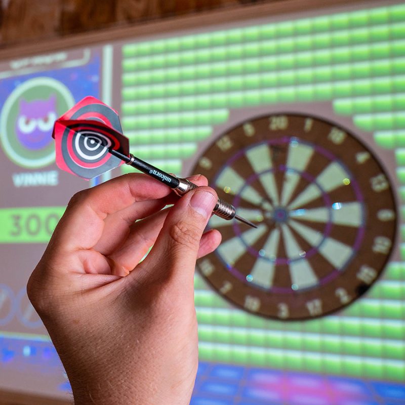 Hand holding a dart aimed at an electronic dartboard.