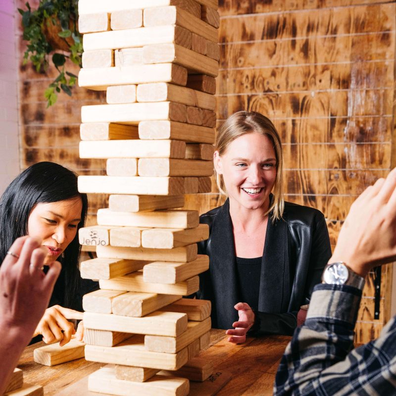 Group of people playing a giant wooden block stacking game at a table.