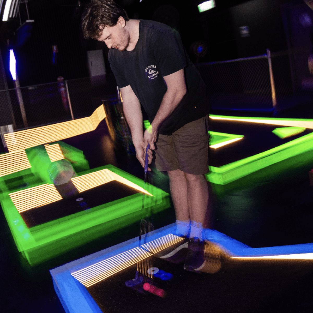 man playing mini golf on indoor neon course