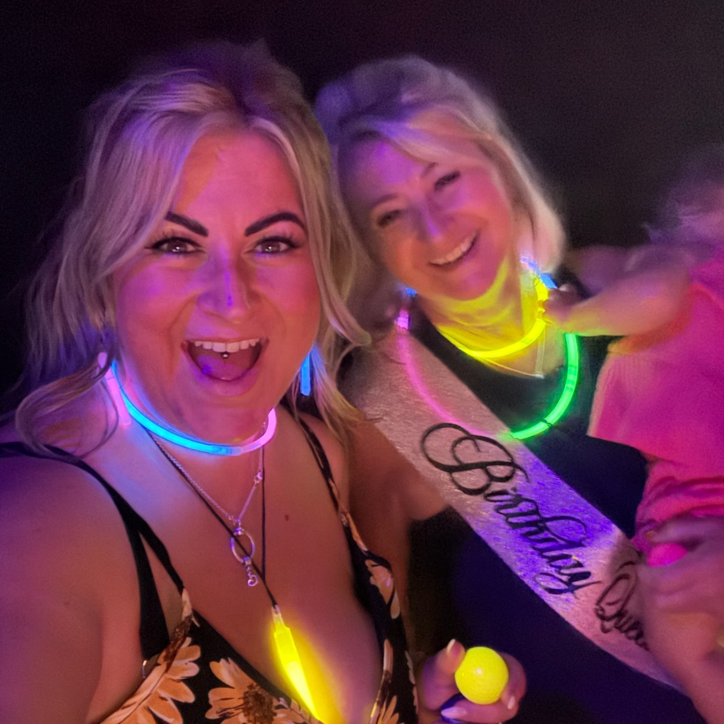 two girls smile in neon while playing glow in the dark mini golf