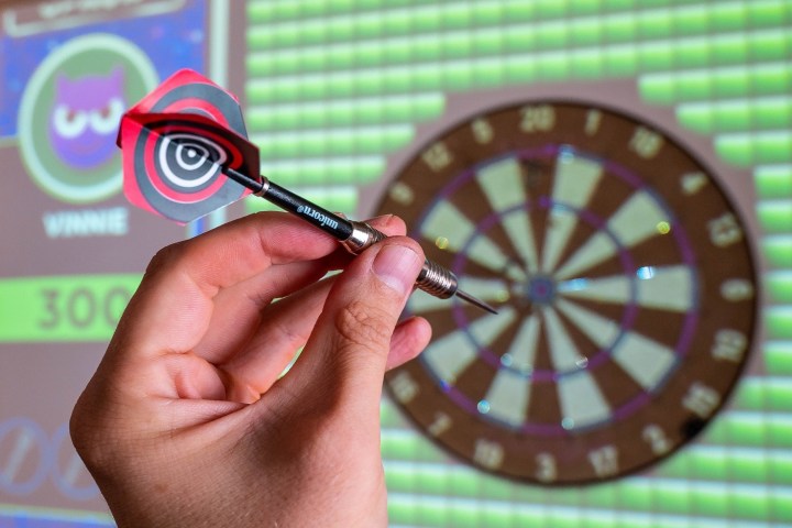 person holding a dart in their left hand with the target in the background