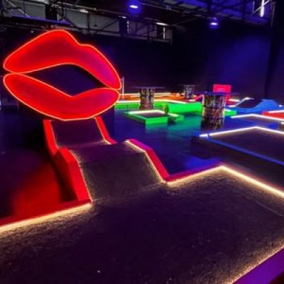 Glow-in-the-dark mini golf course with neon lips and colorful obstacles.