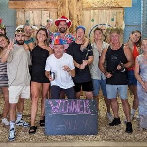 Group of people in festive hats posing with a 'Winner' sign indoors.