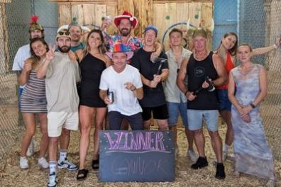 Group of people in festive hats posing with a 'Winner' sign indoors.