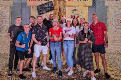 Group of people holding axes at an axe-throwing venue, smiling and posing for a photo.