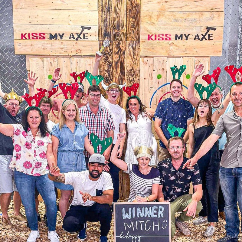 Group of people wearing antler headbands and costumes posing at an axe throwing venue with 'Winner Mitch' sign.