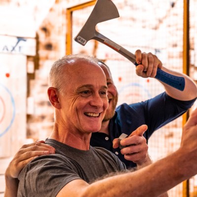 Two men taking a selfie at an axe throwing venue, one holding an axe over the other's head.