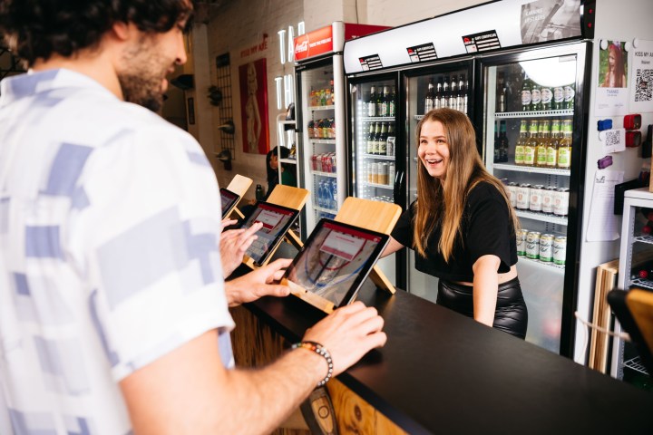 Smiling woman cashier and customer with tablet at beverage store counter.