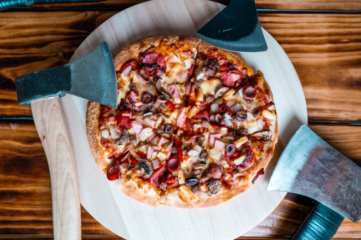 Pizza with various toppings on a wooden board, surrounded by three axes.