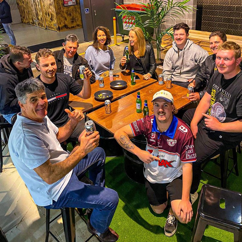 Group of people sitting outdoors at a table, holding drinks, smiling.