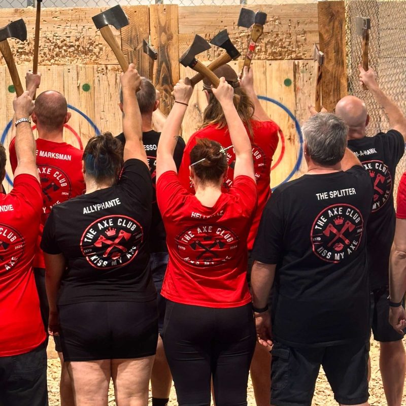 Group of people with axes facing a wooden target wall.
