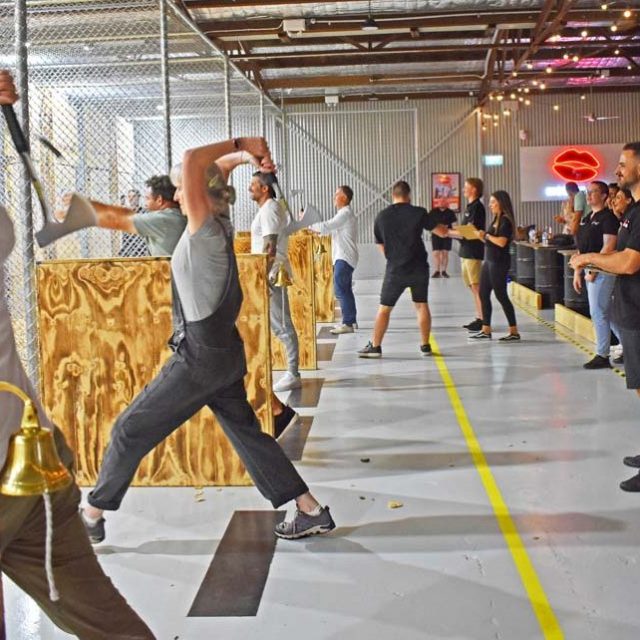 People axe throwing in an indoor range with wood targets and cages.