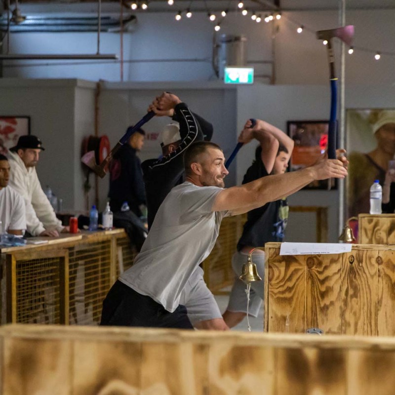 People competing in an indoor axe-throwing event with wooden targets.