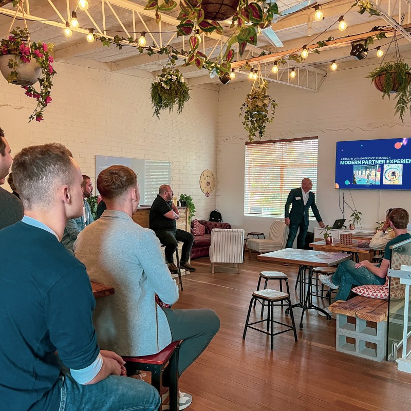 People in a modern room attending a presentation with plants and warm lighting.