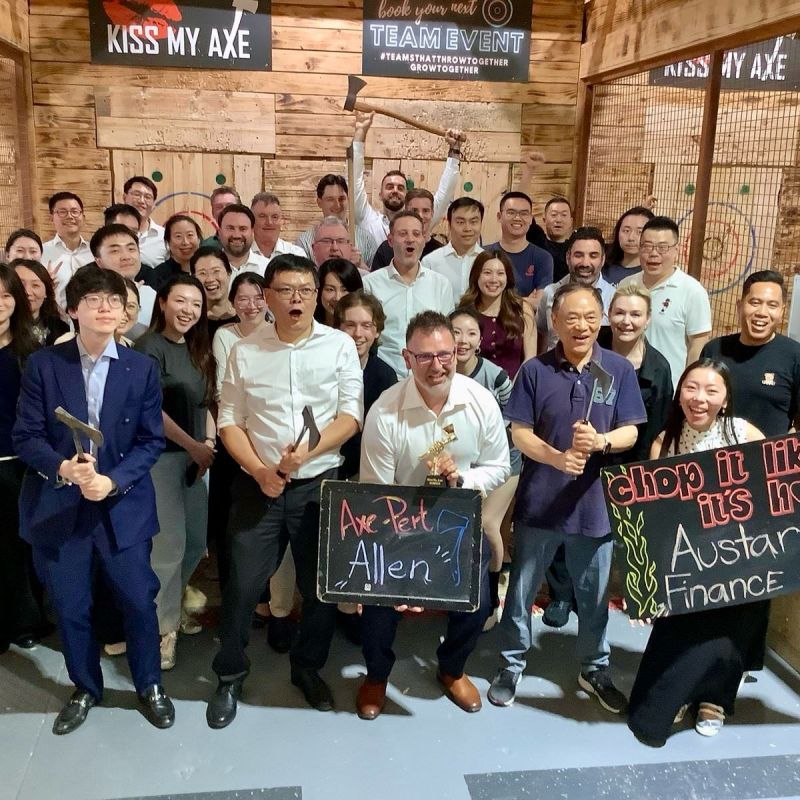Group posing at axe throwing venue holding signs and small axes, with wooden targets in the background.
