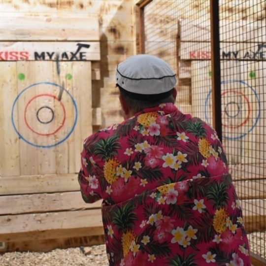 Person in floral shirt throwing an axe at a wooden target indoors.