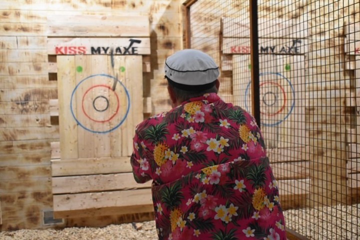 Person in floral shirt throwing an axe at a wooden target indoors.