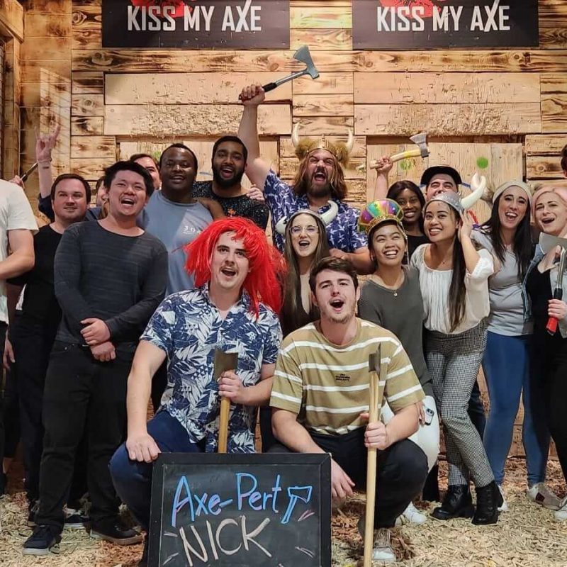 Group of smiling people posing with axes in an axe-throwing venue.
