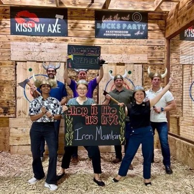 Group of people joyfully posing with axes at an indoor axe-throwing venue.