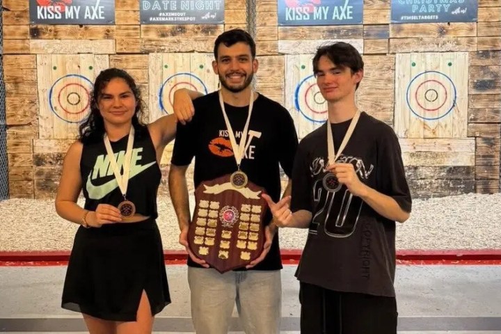 Three people with medals stand in front of axe-throwing targets.