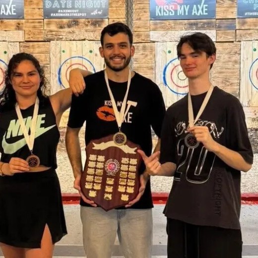 Three people with medals stand in front of axe-throwing targets.