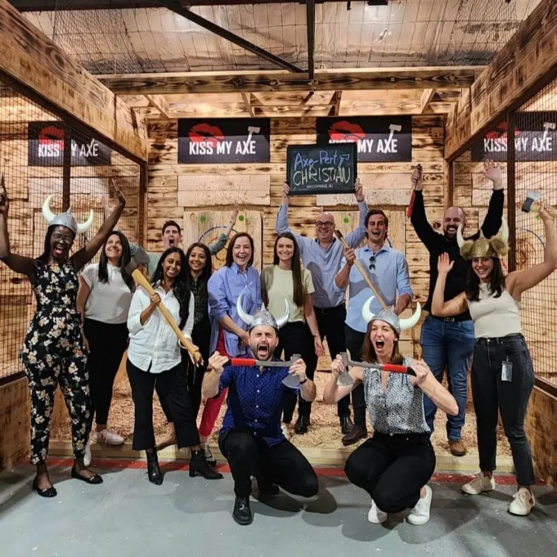 Group of people posing with axes and Viking helmets at an axe-throwing venue indoors.