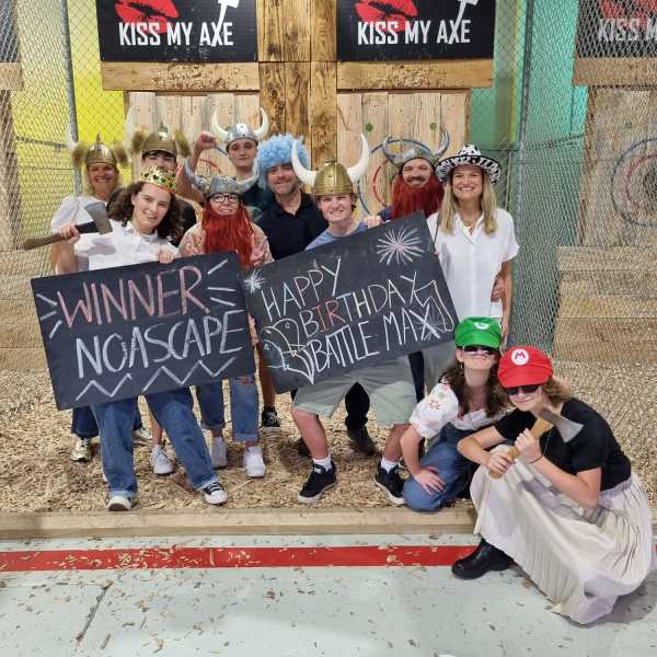 Group celebrating in front of axe throwing targets with signs and costumes.