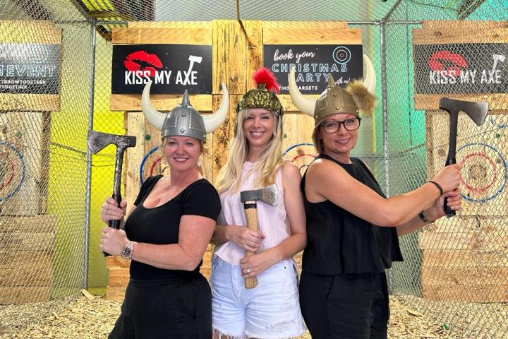 Three people wearing Viking helmets holding axes at an axe-throwing venue.