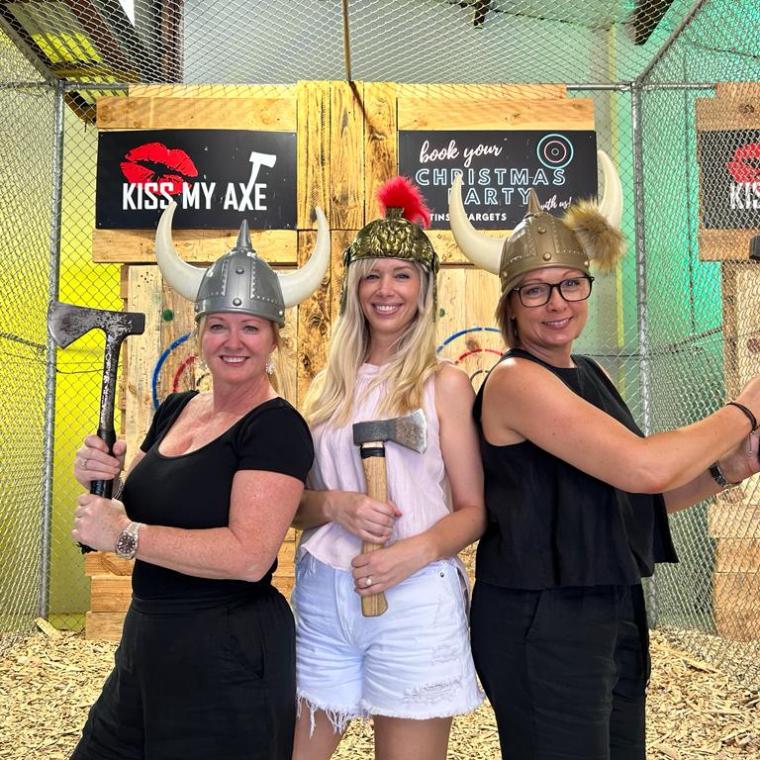 Three people wearing Viking helmets holding axes at an axe-throwing venue.