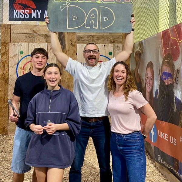 Happy family posing with 'Winner Dad' sign at an axe-throwing venue.