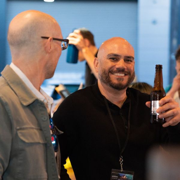 Two men smiling and holding drinks at a casual indoor event.