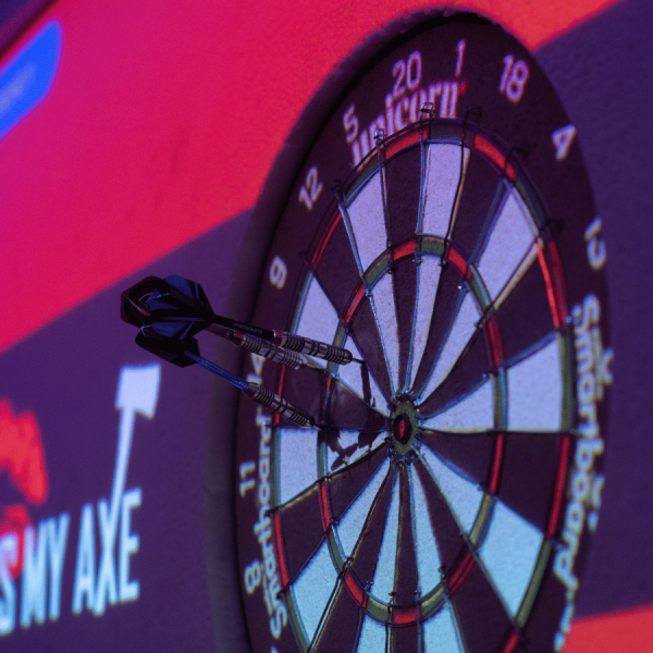 Dartboard with darts and 'Kiss My Axe' logo in the background.
