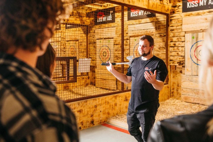 Man instructing axe throwing session in wooden indoor venue.