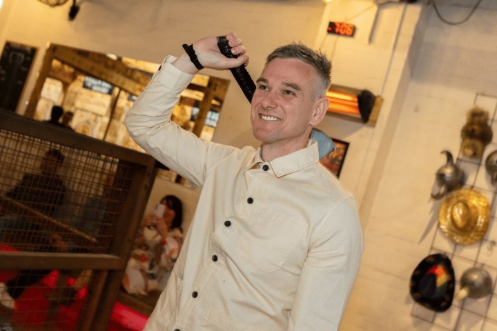 Person in beige jacket holding an axe in an indoor setting.