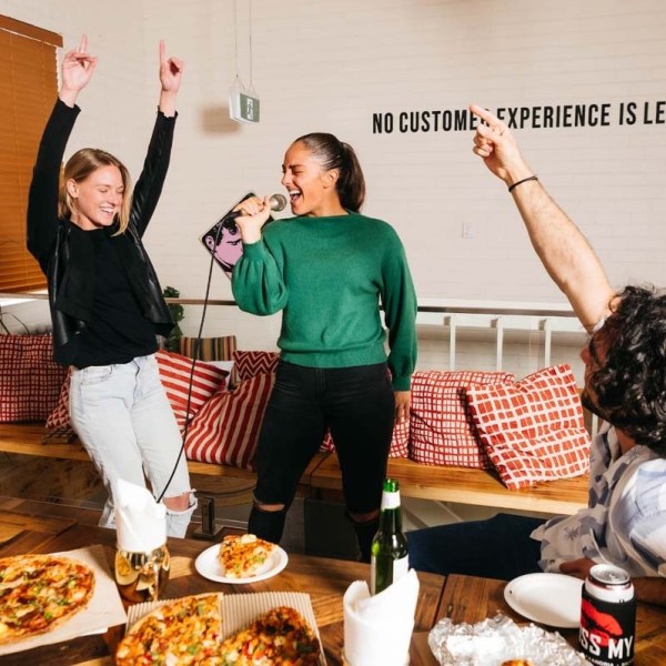 People enjoying karaoke with pizza and drinks in a lively room.
