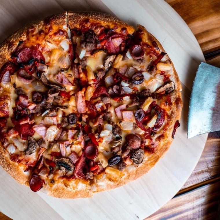 Pizza with toppings next to an axe on a wooden table.