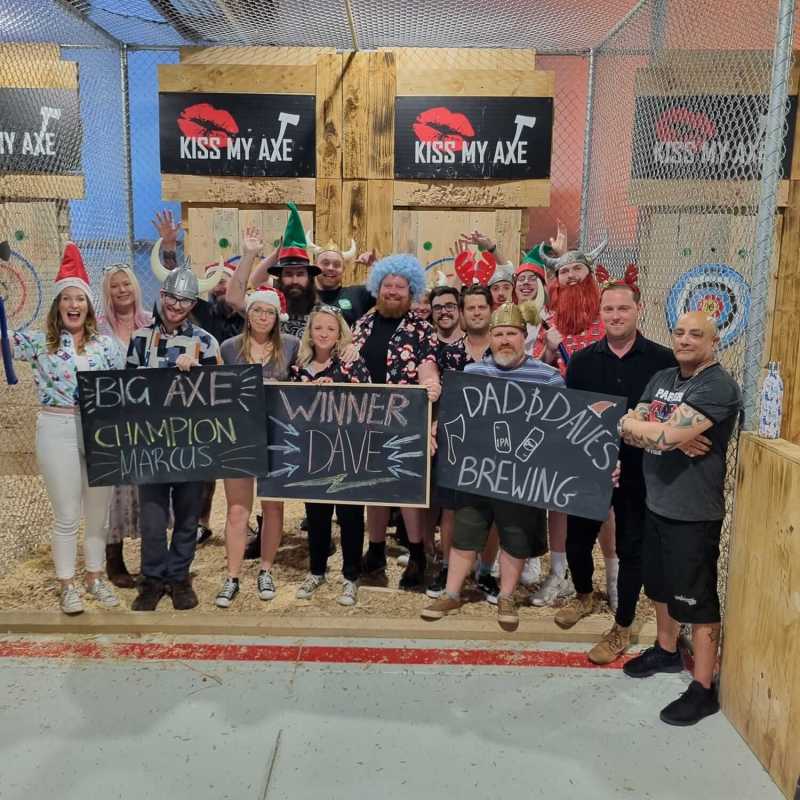 Group of people holding signs in an axe-throwing venue with bullseyes in the background.