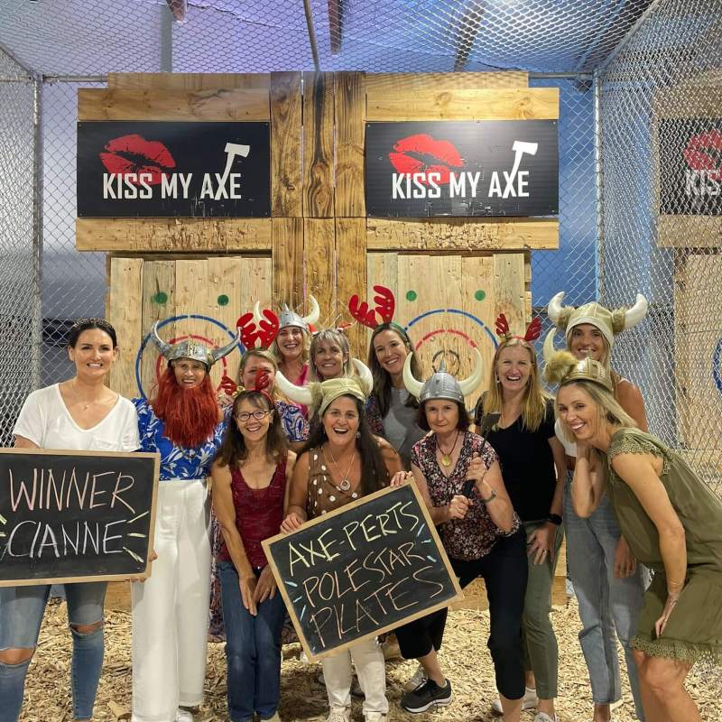 Group posing with signs and costumes at an axe-throwing venue.