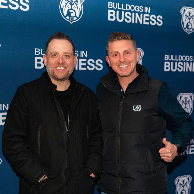 Two men smiling in front of a 'Bulldogs in Business' backdrop.