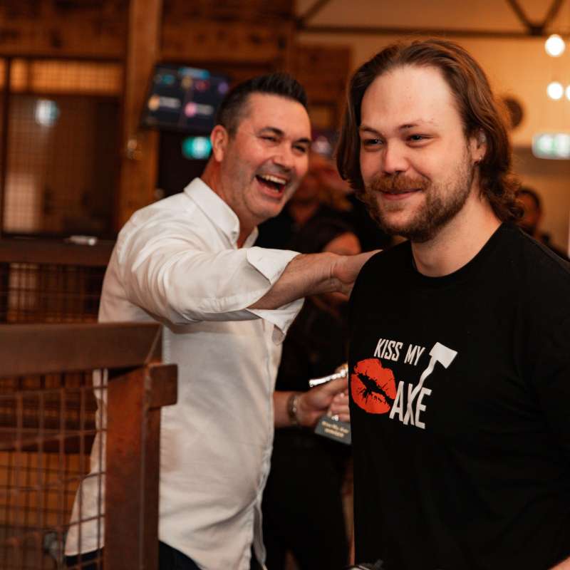 Man in black shirt smiling, man in white shirt laughing in a lively indoor setting.