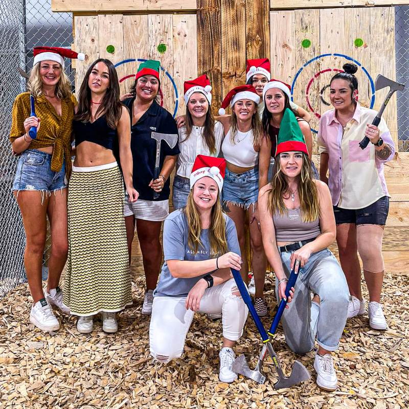 Group of people in Santa hats holding axes in an axe-throwing venue.