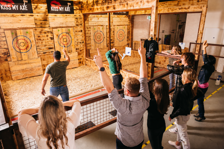 People watching a man throw an axe at a bullseye target in a wooden indoor arena.