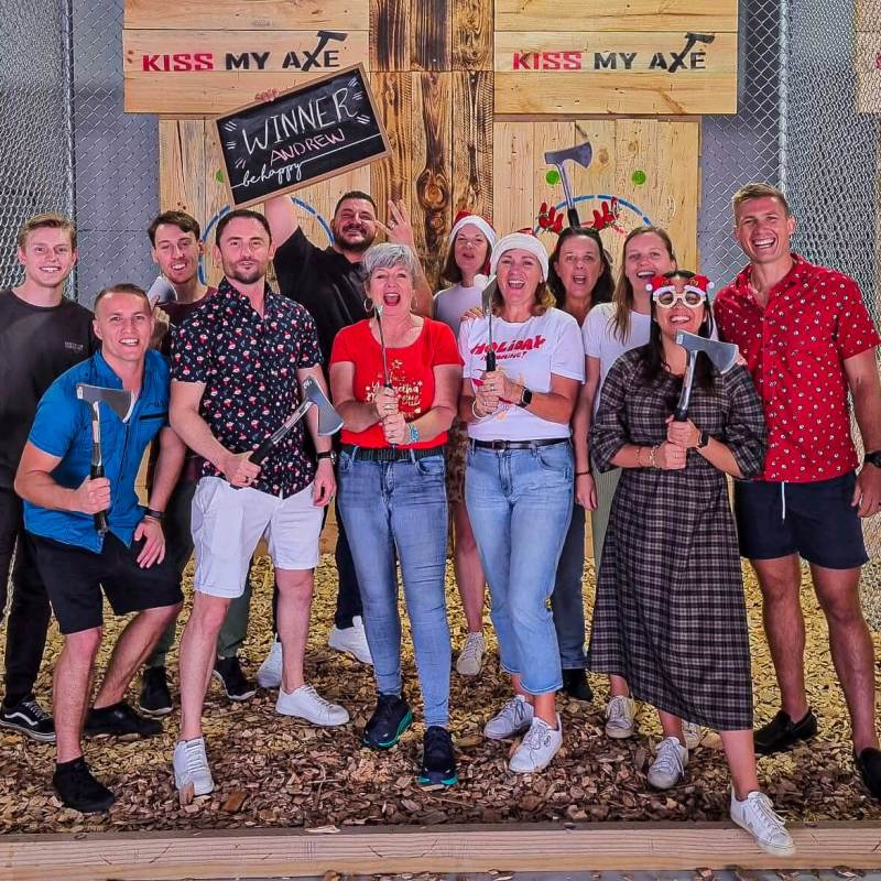 Group of people posing with axes at a throwing venue.