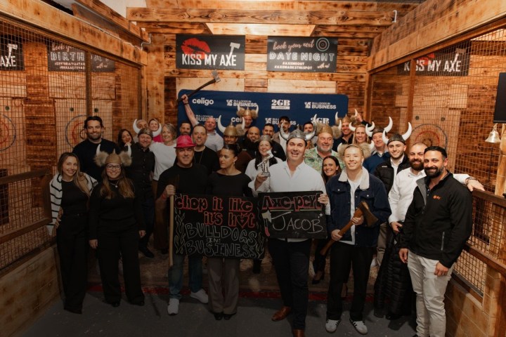 Group photo in wooden room with people holding axes, wearing helmets, and smiling.