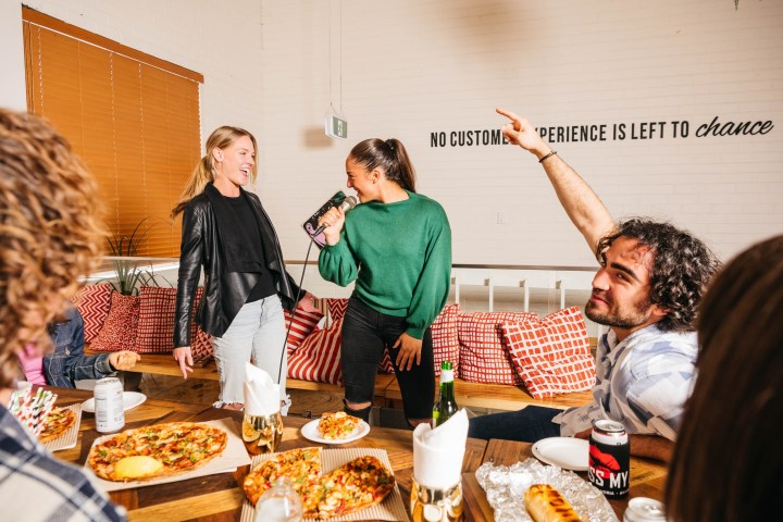 People having fun, singing karaoke at a table with pizza and drinks.