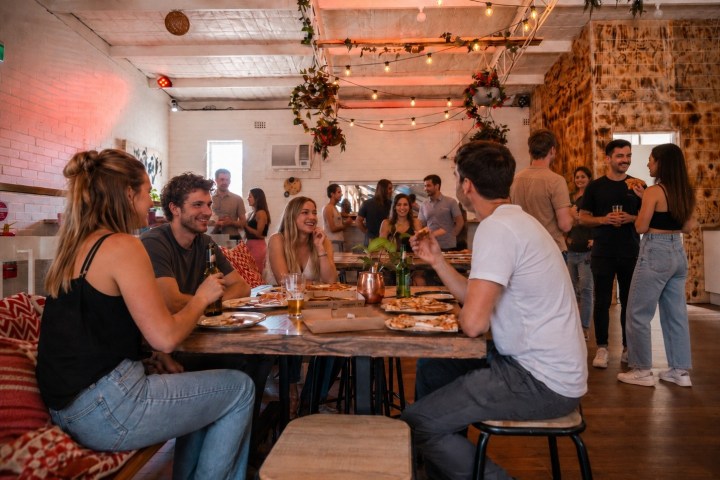 Group of people socializing in a warmly lit room with tables and hanging lights.