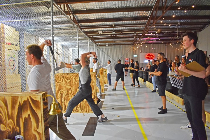 People axe throwing in an indoor venue with spectators watching.