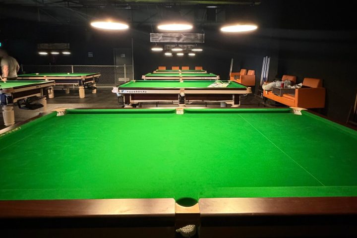 Dimly lit pool hall with green tables and overhead lights.