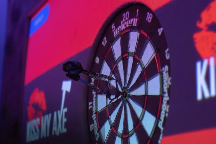 Dartboard with two darts, logo and text on wall in background.